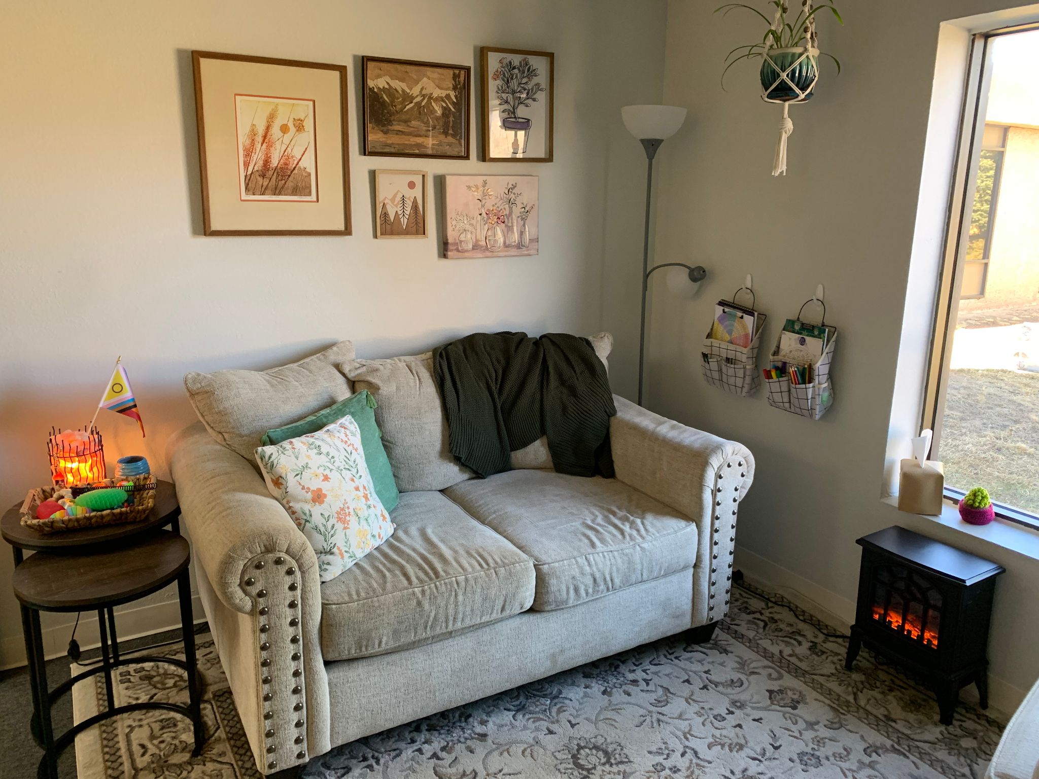 cream-colored couch with throw pillows on a blue rug next to an electric fireplace and window