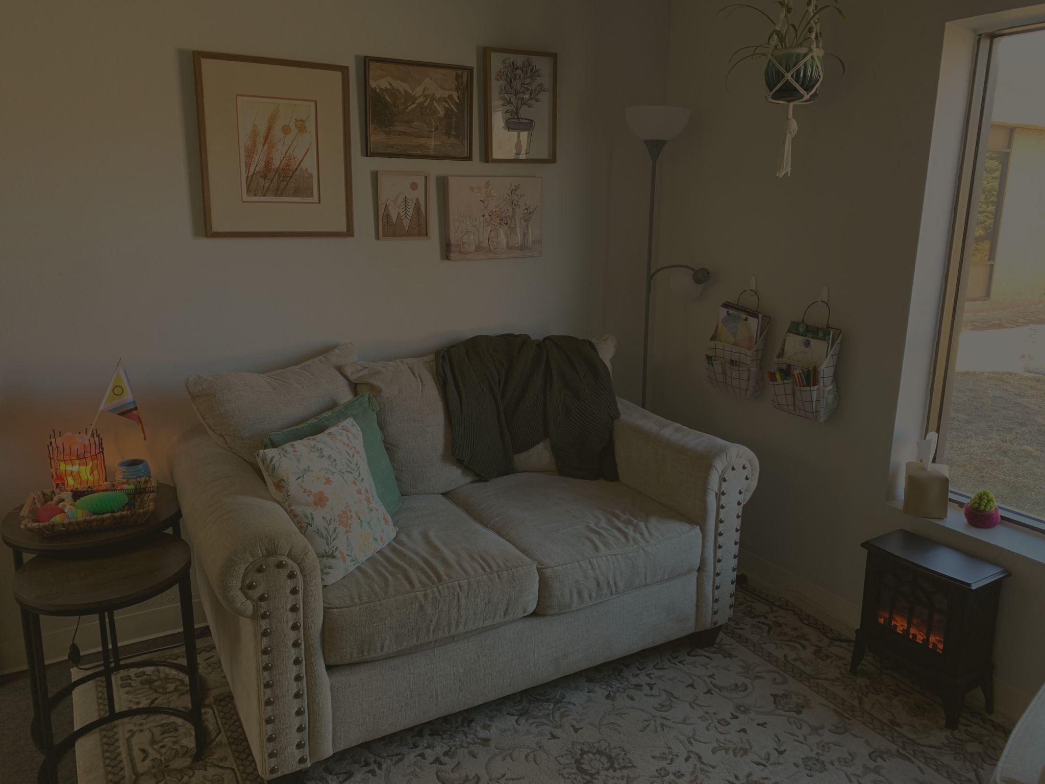 cream-colored couch with throw pillows on a blue rug next to an electric fireplace and window
