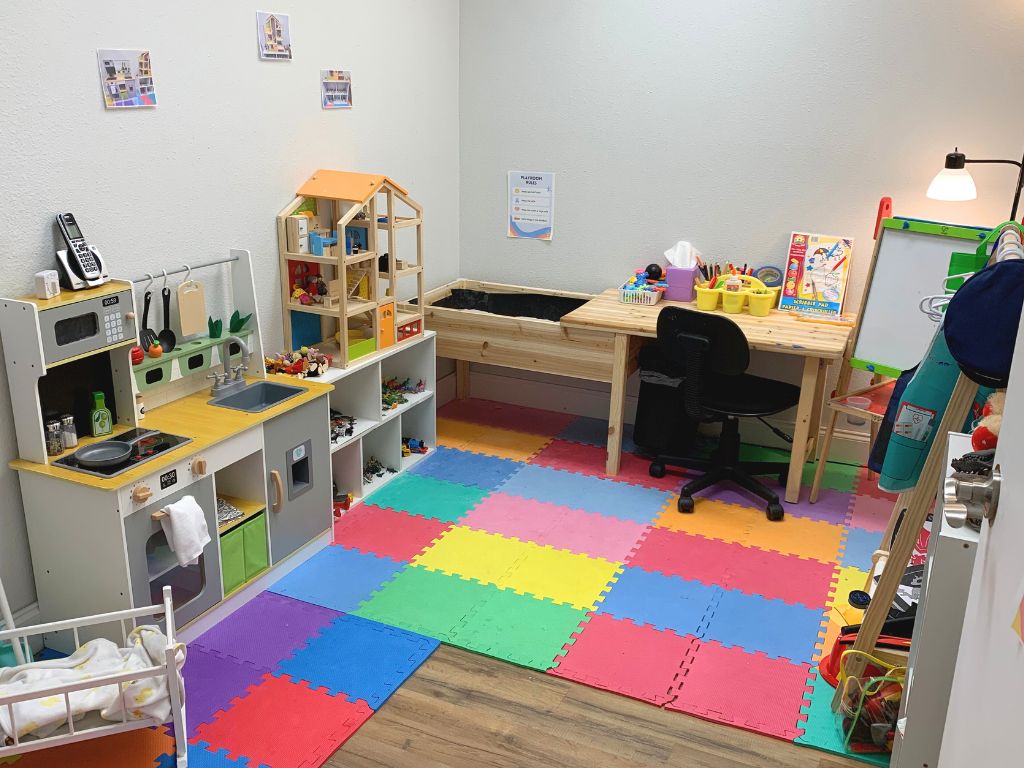 child therapy room with toy kitchen, foam floor mats, and a wooden desk