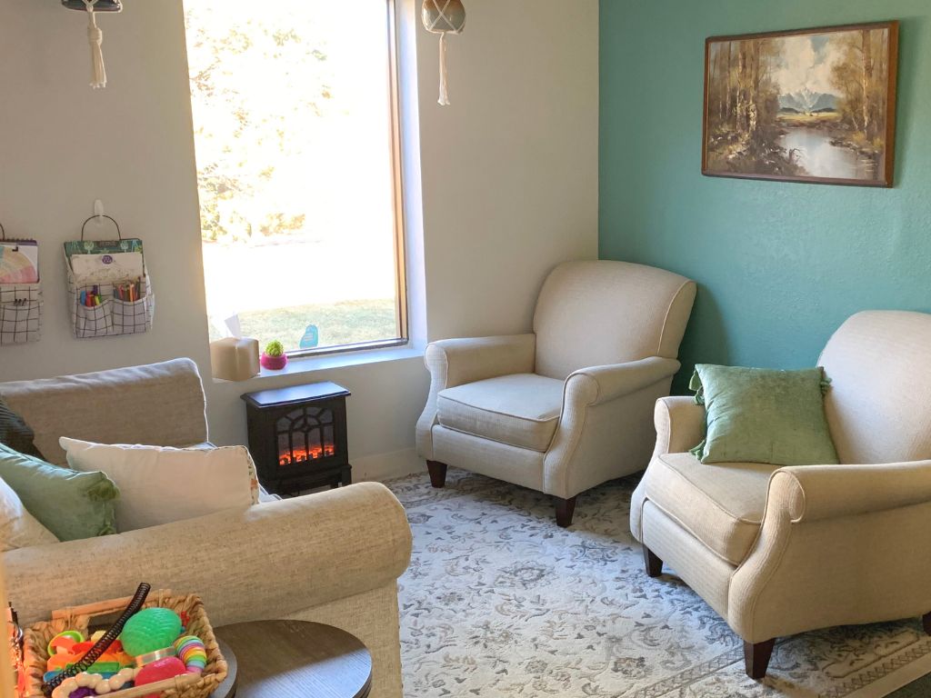 Office for therapy with blue and cream walls, cream couch and two chairs, on a cream rug in front of an electric fireplace