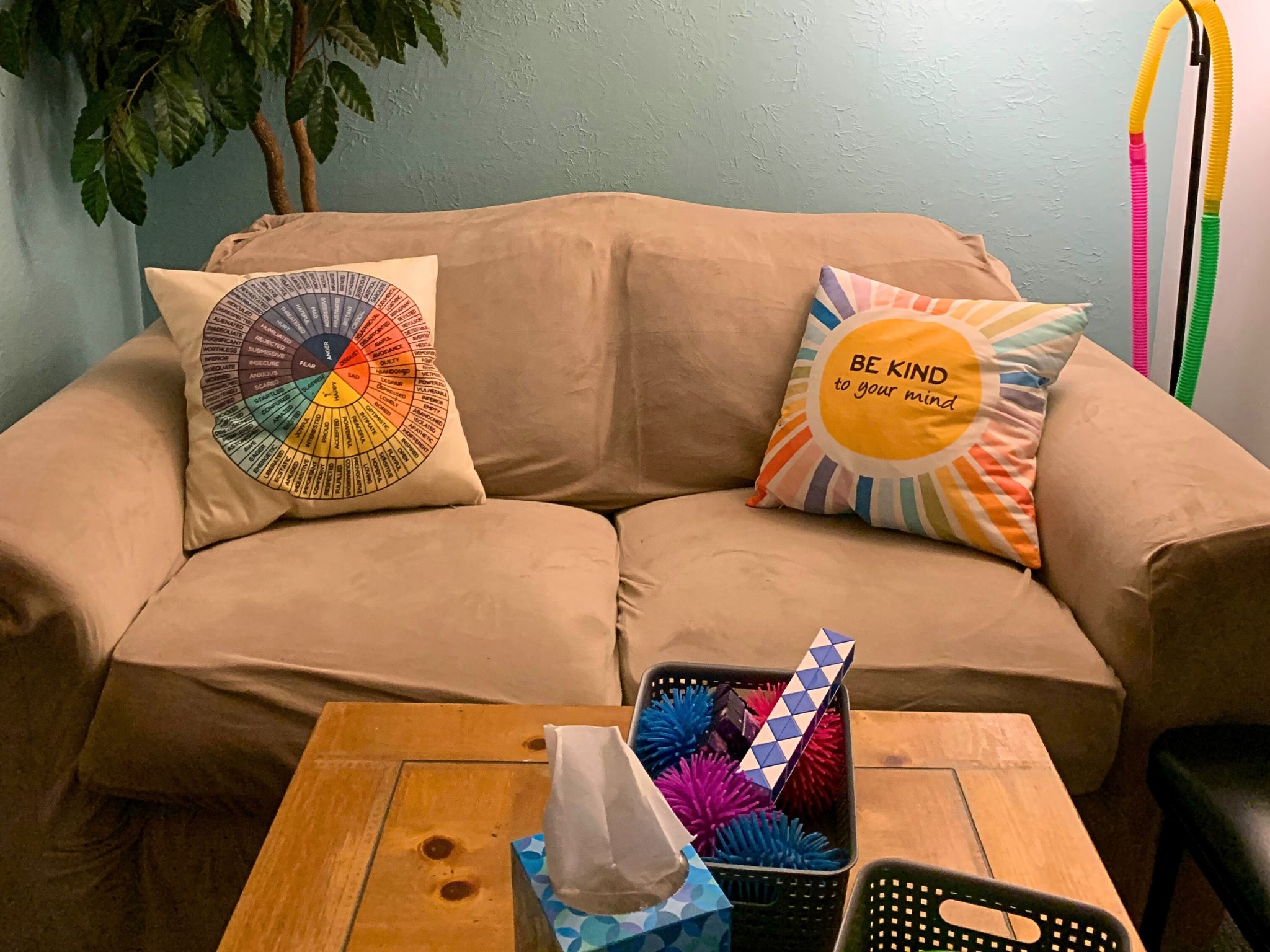 Teen Room therapy office with cream couch and colorful pillows in front of a wooden coffee table