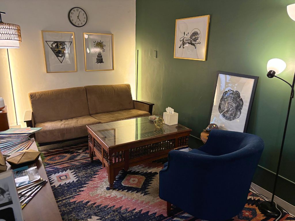 Office space for therapy with a brown couch facing a blue chair, with a cream wall and a green wall
